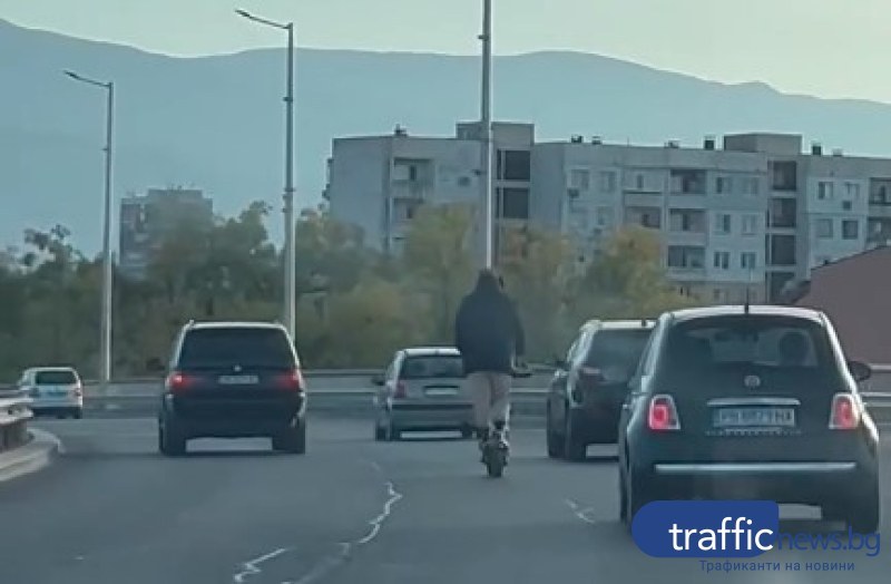 Мъж и жена се движат сред колите, качени заедно на тротинетка в Пловдив